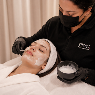 Profesional de Glow Beauty Bar aplicando una mascarilla facial con pincel durante el tratamiento.
